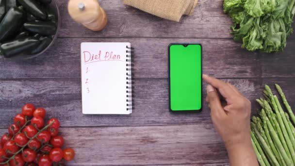 Vue du dessus de mans main tenant téléphone intelligent avec des légumes frais sur la table — Video