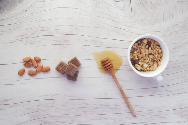 Pequeno-almoço de cereais em taça, noz de amêndoa. chocolate e mel na mesa — Fotografia de Stock