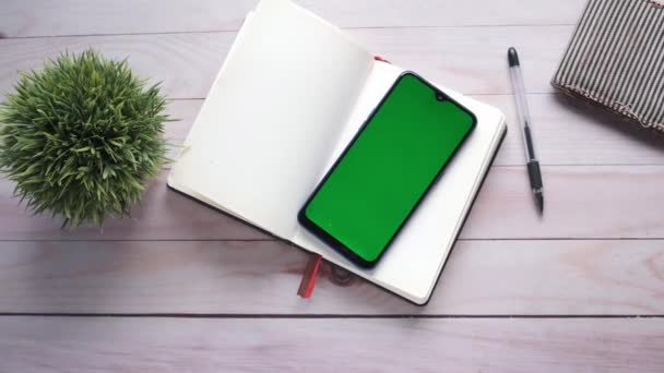 Вид зверху смартфона з зеленим екраном і блокнотом на столі — стокове відео