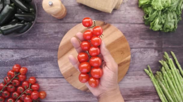 Hand houden kleurrijke cherry tomaat tegen houten tafel — Stockvideo