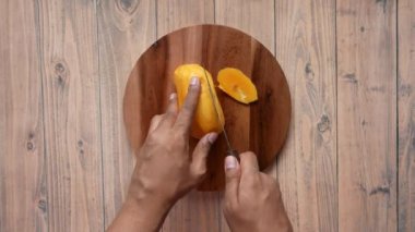 Olgun mangoyu doğrama tahtasıyla kesen genç adamın üst görüntüsü. 