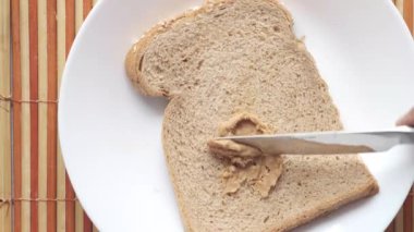 Fıstık ezmesinin üst görüntüsü ve siyah arka planda bir tabak ekmek. 