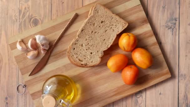 Bovenaanzicht van brood, knoflook, tomaat en olijfolie op tafel — Stockvideo