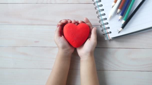 Ребенок держит красное сердце на столе — стоковое видео