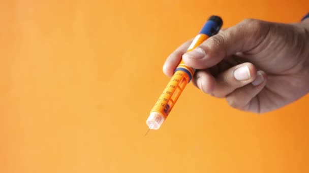 Hand hält Insulin-Stifte vor orangefarbenem Hintergrund — Stockvideo