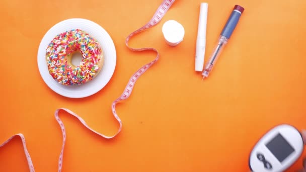 Діабетичні засоби вимірювання, інсулін та пончики на помаранчевому фоні — стокове відео