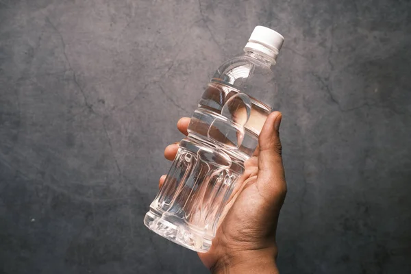 La celebración de la mano de la botella de agua potable sobre fondo negro — Foto de Stock