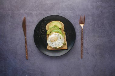 Avokado, kahverengi ekmek, yumurta ve siyah arka planda biberiye. 