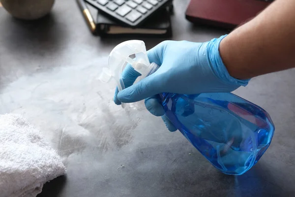 Hand in blauwe rubberen handschoenen met spuitfles reinigingstafel — Stockfoto