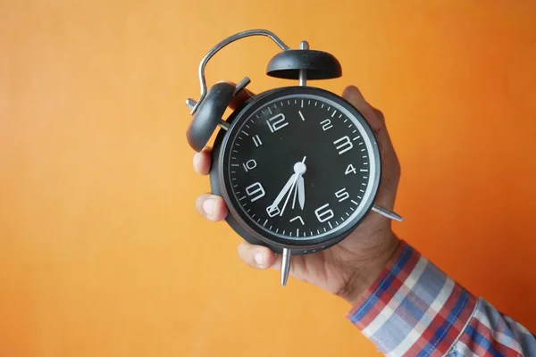 Mano de la persona que sostiene el reloj despertador contra fondo naranja , —  Fotos de Stock