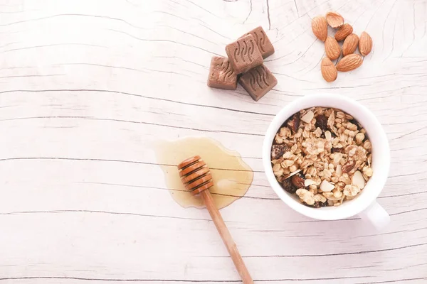 Pequeno-almoço de cereais em tigela, mel, amêndoa e chocolate sobre fundo branco — Fotografia de Stock