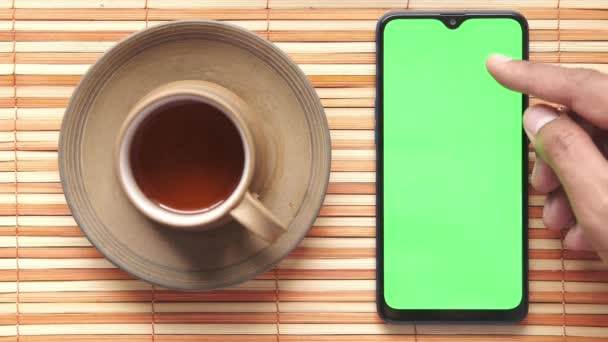 Mano joven usando teléfono inteligente con té y galletas en la mesa — Vídeo de stock