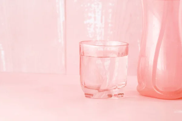 Glas Wasser und Kunststoffbehälter auf rosa — Stockfoto