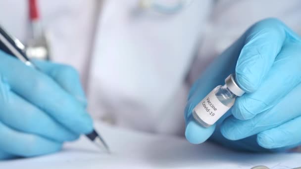 Mână în mănuși din latex care țin vaccinul fiolă de sticlă și scriu pe hârtie — Videoclip de stoc