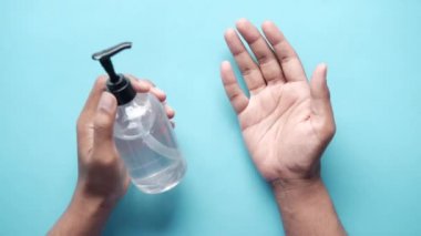 Mavi zemin üzerinde dezenfektan sıvısı kullanan bir adamın üst görünümü 