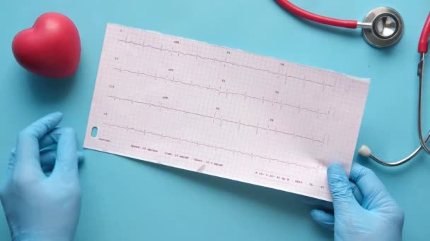 Arzt Hand in Hand mit medizinischen Handschuhen bei der Analyse des Kardiodiagramms. — Stockvideo