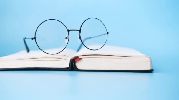 Open book, and a eyeglass on blue background — Stock Video