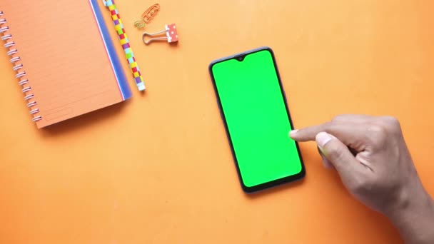 Junger Mann scrollt Smartphone auf orangefarbenem Hintergrund — Stockvideo