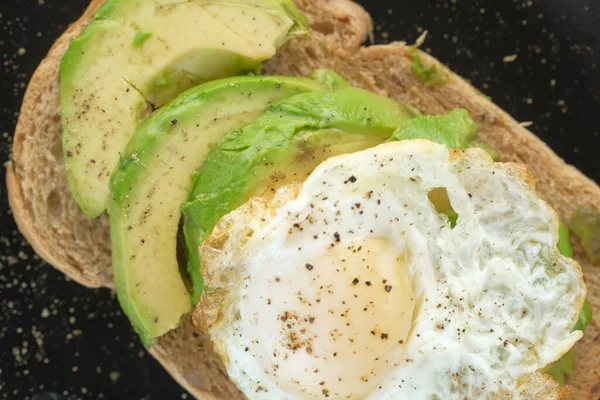 Avokado, kahverengi ekmek, yumurta ve biberiye masada.