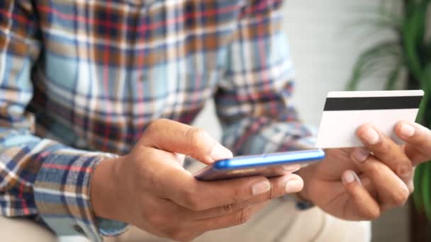 Fiatal férfi üzembe hitelkártya részleteket okos telefon, miközben ül — Stock videók