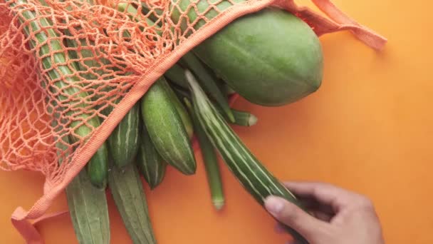 Ta ut grönsaker ur återanvändbar påse på orange bakgrund — Stockvideo