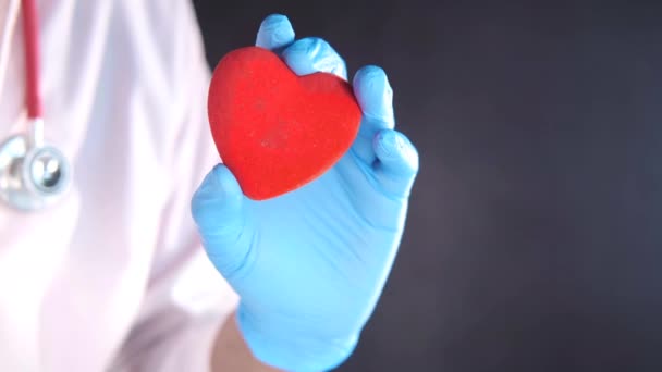 Mano de hombre en guantes protectores que sostienen el corazón rojo contra fondo negro — Vídeo de stock