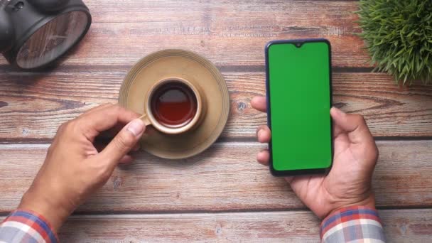 Молодой человек протягивает смартфон с чаем и кулинарией на столе — стоковое видео