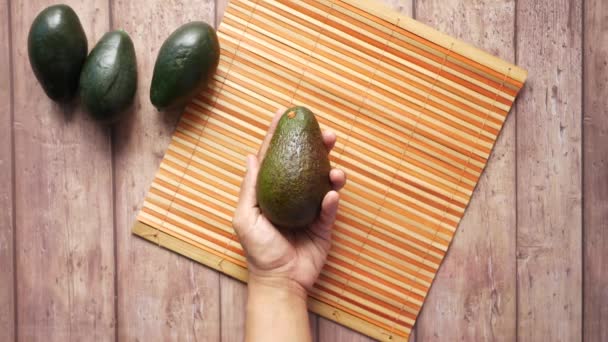 Рука тримає шматочок авокадо на дерев'яному столі — стокове відео