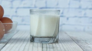 Bir kasede yumurta ve masada bir bardak süt. 