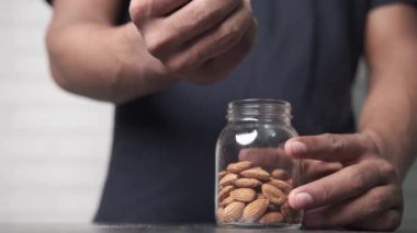 Genç adam cam bir şişeye badem fıstığı dolduruyor. 