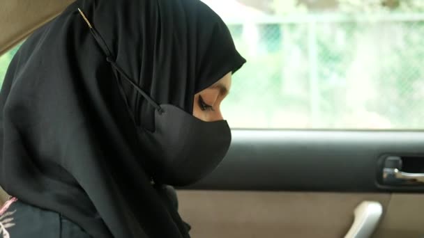 Vista lateral da mulher muçulmana com máscara de gripe olhando através de uma janela do carro — Vídeo de Stock