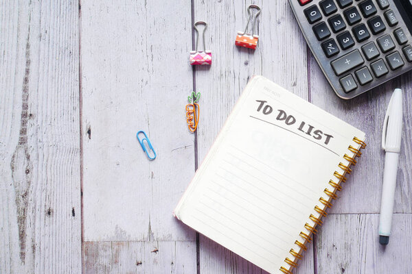 To do list in notebook with office suppliers on desk.