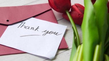 Teşekkür mesajı, zarf ve lale çiçeği masada. 