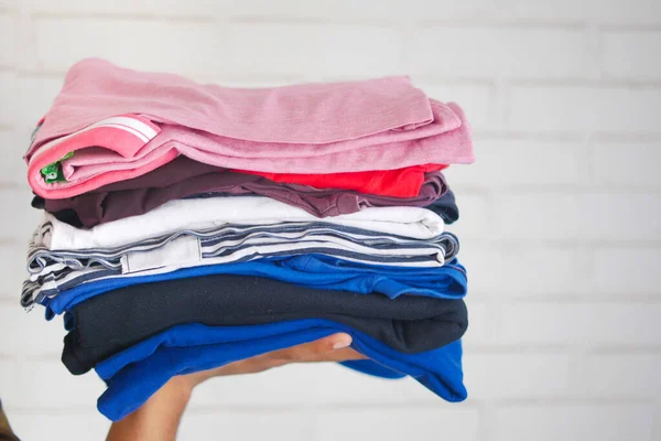 Hand houden stapel kleding tegen een muur achtergrond — Stockfoto