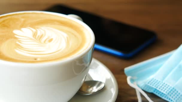 Uma xícara de café tarde, telefone e máscara cirúrgica na mesa — Vídeo de Stock