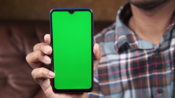 Hombre joven sosteniendo el teléfono inteligente con pantalla verde interior — Vídeos de Stock