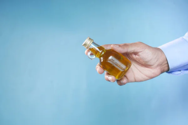 Mano sosteniendo una botella de aceite de oliva sobre fondo azul — Foto de Stock