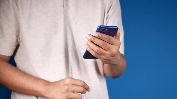 Junger Mann bedient Smartphone vor blauem Hintergrund — Stockvideo