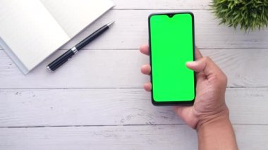 Genç adam yeşil ekranlı akıllı bir telefon tut. Masada not defteri ve kalem olsun. 