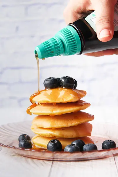 Menuangkan sirup maple di pancake dengan buah segar di piring — Stok Foto