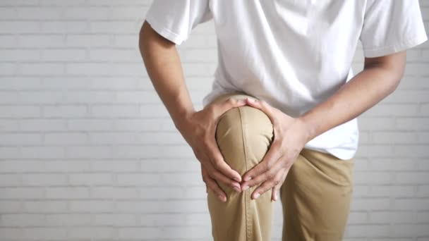 Hombre que sufre dolor en las articulaciones de la rodilla de pie contra pared blanca — Vídeos de Stock