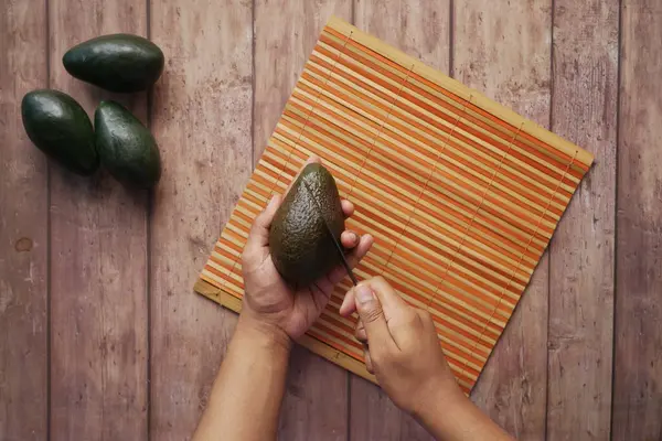 Hand skära skiva av avokado på träbord — Stockfoto
