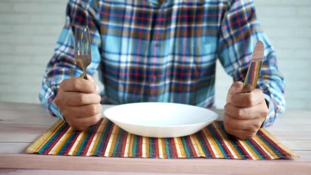 Hand holding cutlery with empty plate on wooden table — Stock Video