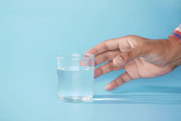 Mão segurando um copo de água contra fundo azul — Fotografia de Stock
