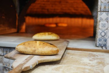 Freshly baked bread rests on a wooden board near a stone oven.