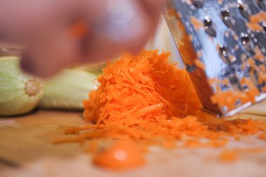 Eller ahşap bir yüzey üzerinde taze yiyecek hazırlayan parlak turuncu havuçları rendeliyor..