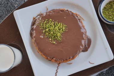 kunafe chocolate dessert with pistachio topping and milk.