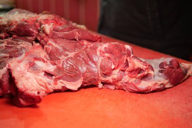 Büyük bir parça çiğ et parlak kırmızı bir masanın üzerinde duruyor..