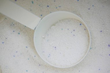 Measuring scoop filled with white laundry detergent on a clean surface.