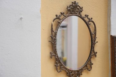 An ornate mirror reflects light against a yellow wall in a cozy room.